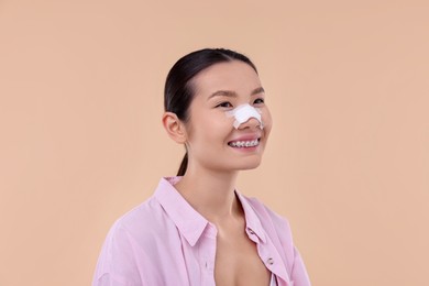 Photo of Woman with medical bandage on her nose after plastic surgery operation against beige background