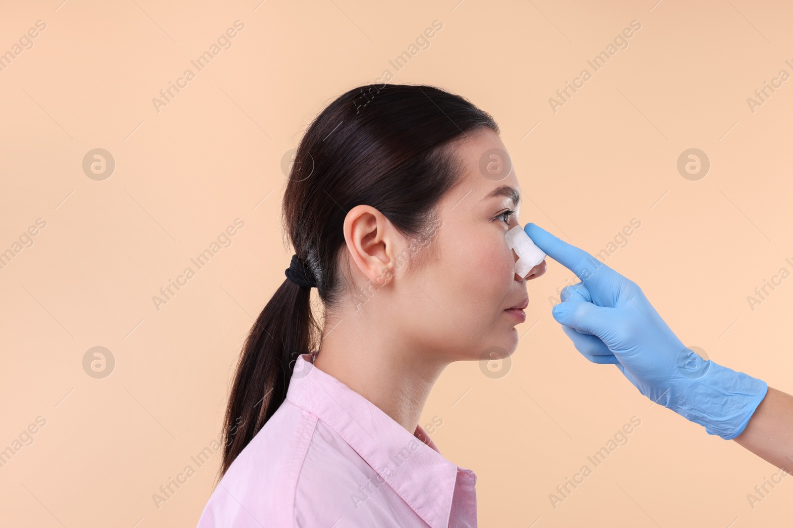 Photo of Doctor checking patient's nose after plastic surgery operation on beige background, closeup