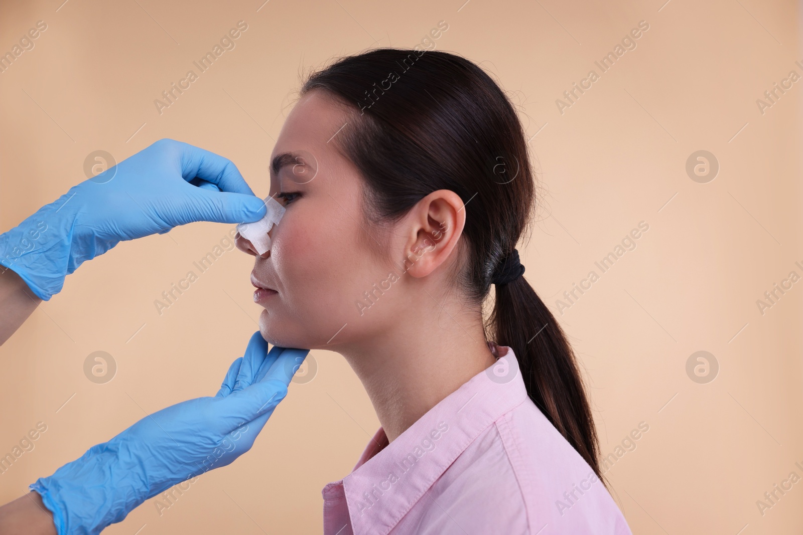 Photo of Doctor checking patient's nose after plastic surgery operation on beige background, closeup