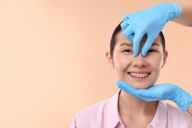 Photo of Doctor checking patient's nose before plastic surgery operation on beige background, closeup. Space for text