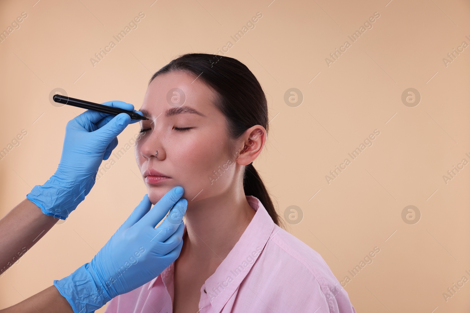 Photo of Doctor drawing marks on patient's nose for plastic surgery operation against beige background, closeup. Space for text