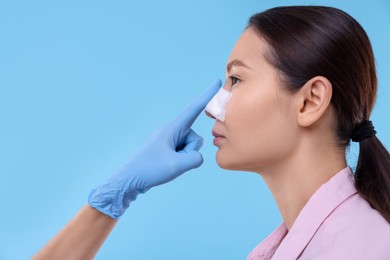 Photo of Doctor checking patient's nose after plastic surgery operation on light blue background, closeup