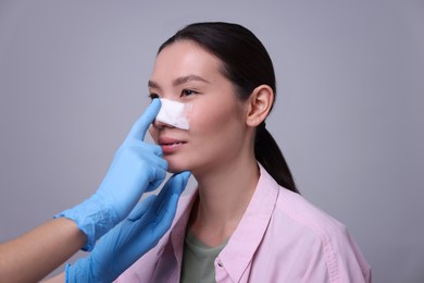 Photo of Doctor checking patient's nose after plastic surgery operation on light grey background, closeup