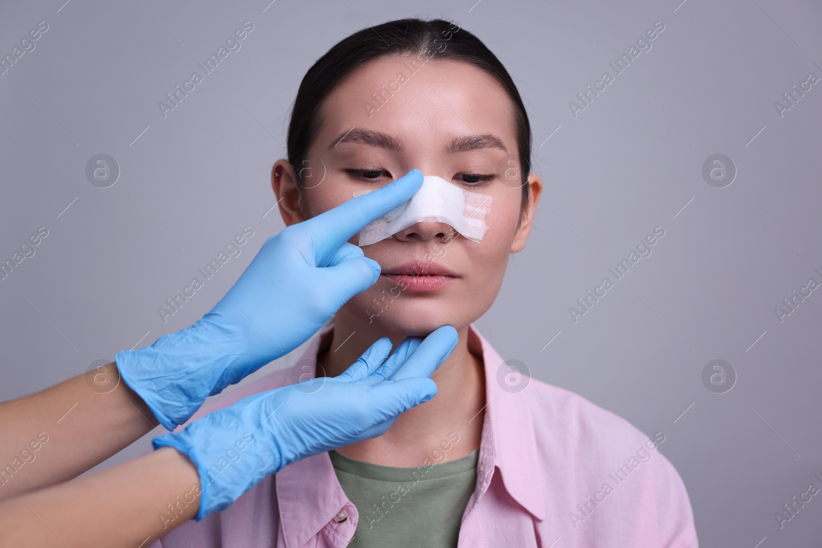 Photo of Doctor checking patient's nose after plastic surgery operation on light grey background, closeup