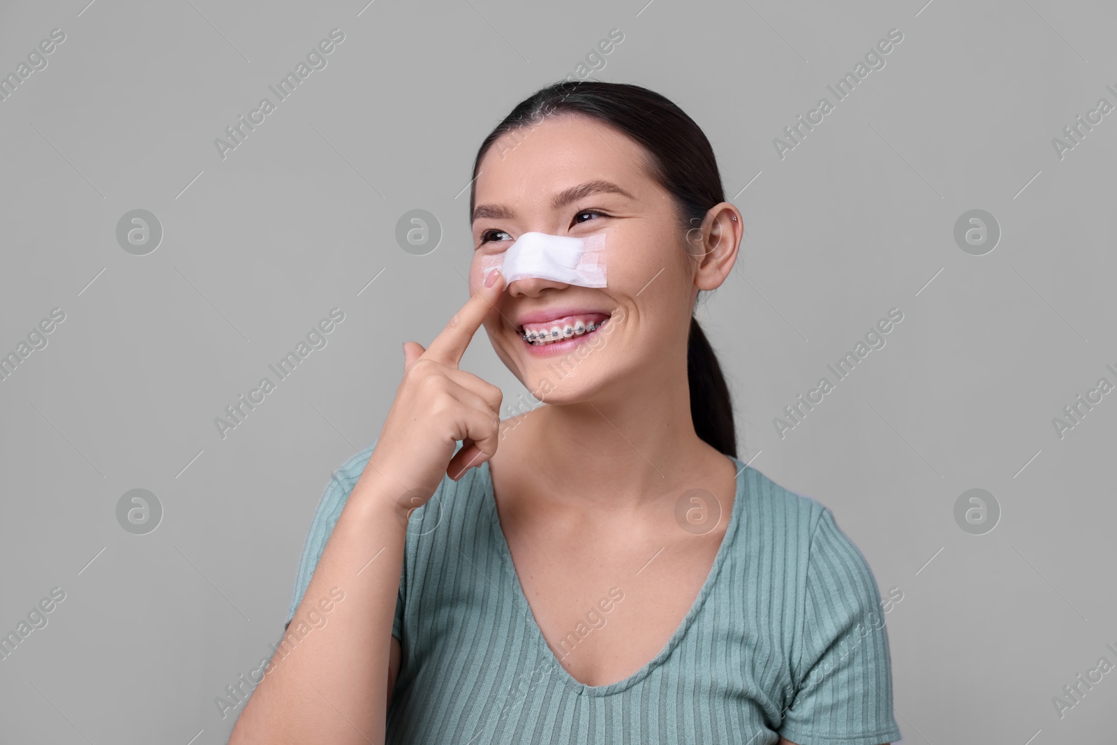 Photo of Woman with medical bandage on her nose after plastic surgery operation against light grey background