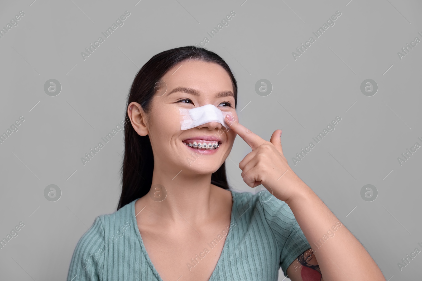 Photo of Woman with medical bandage on her nose after plastic surgery operation against light grey background