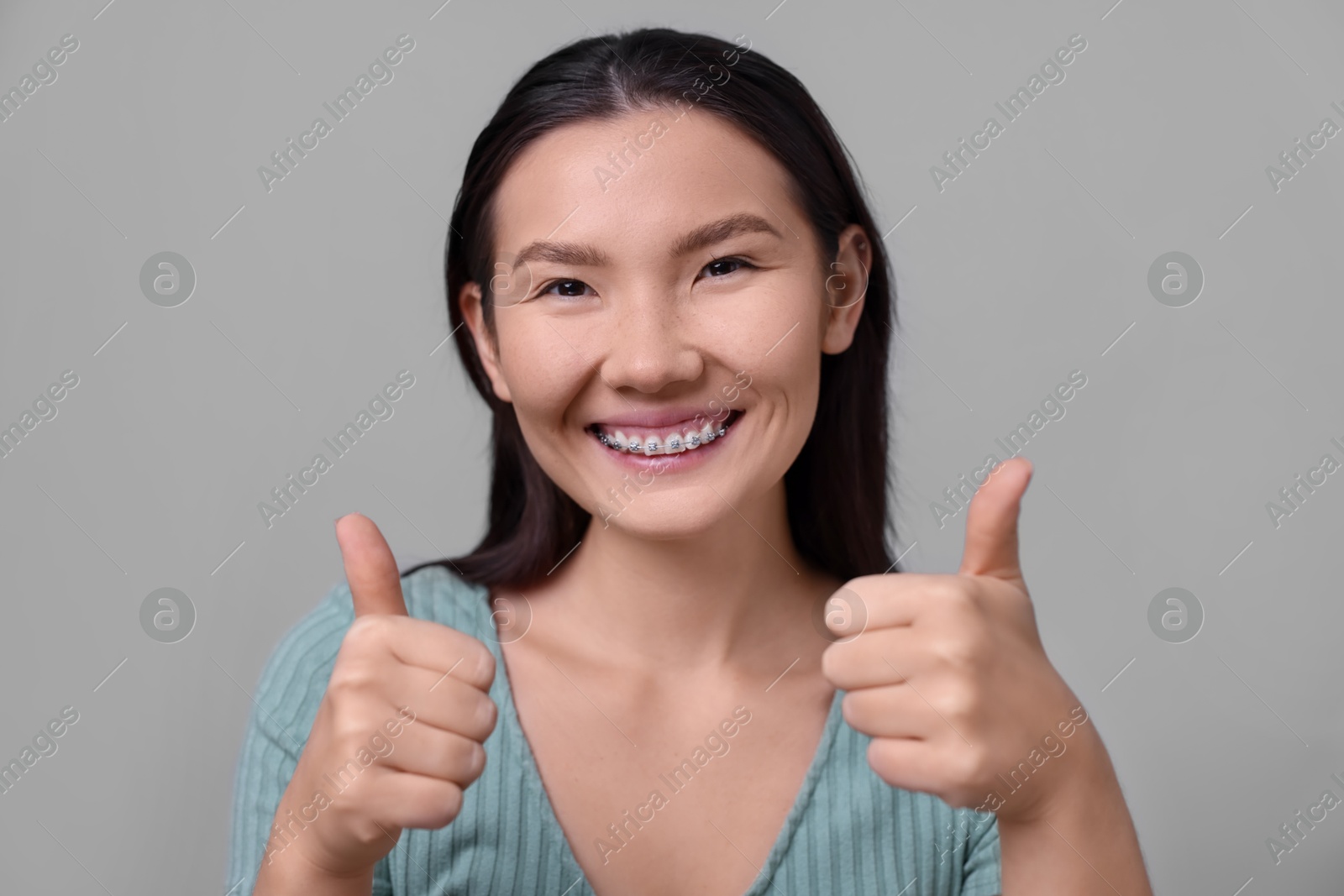 Photo of Woman with beautiful nose showing thumbs up on light grey background. Rhinoplasty surgery