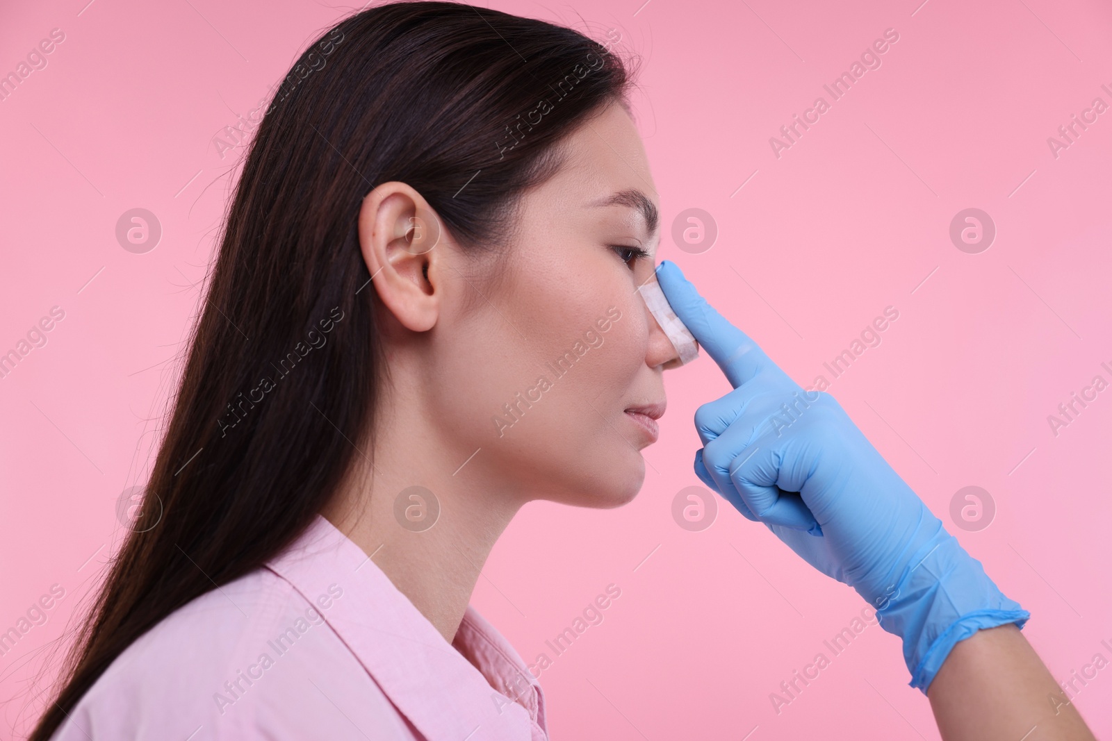 Photo of Doctor checking patient's nose after plastic surgery operation on pink background, closeup