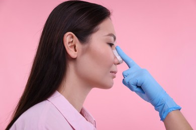 Photo of Doctor checking patient's nose after plastic surgery operation on pink background, closeup