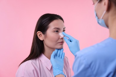 Photo of Doctor checking patient's nose after plastic surgery operation on pink background