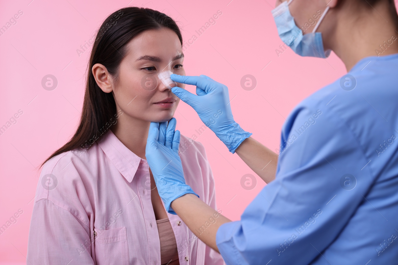 Photo of Doctor checking patient's nose after plastic surgery operation on pink background