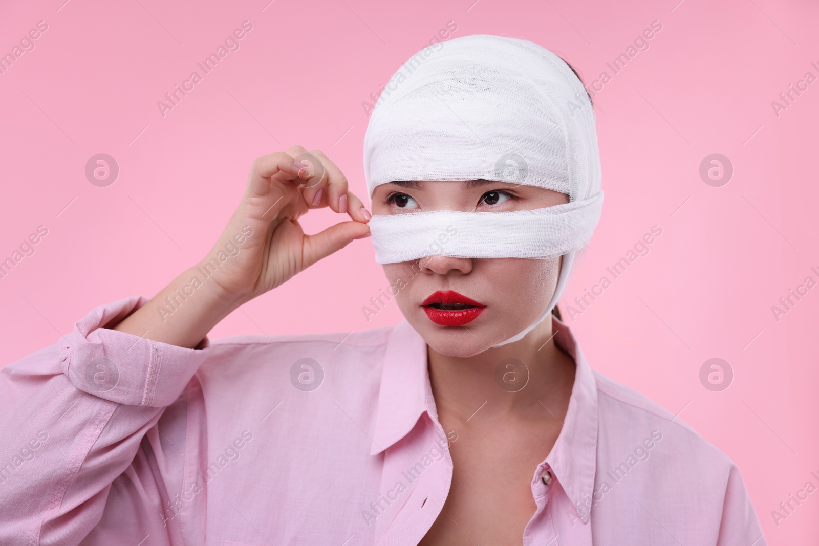 Photo of Woman with nose wrapped in medical bandage after plastic surgery operation on pink background