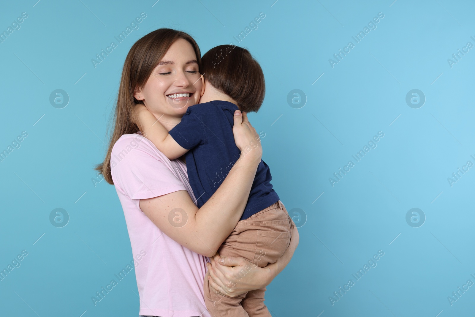 Photo of Happy mother with her cute little son on light blue background, space for text