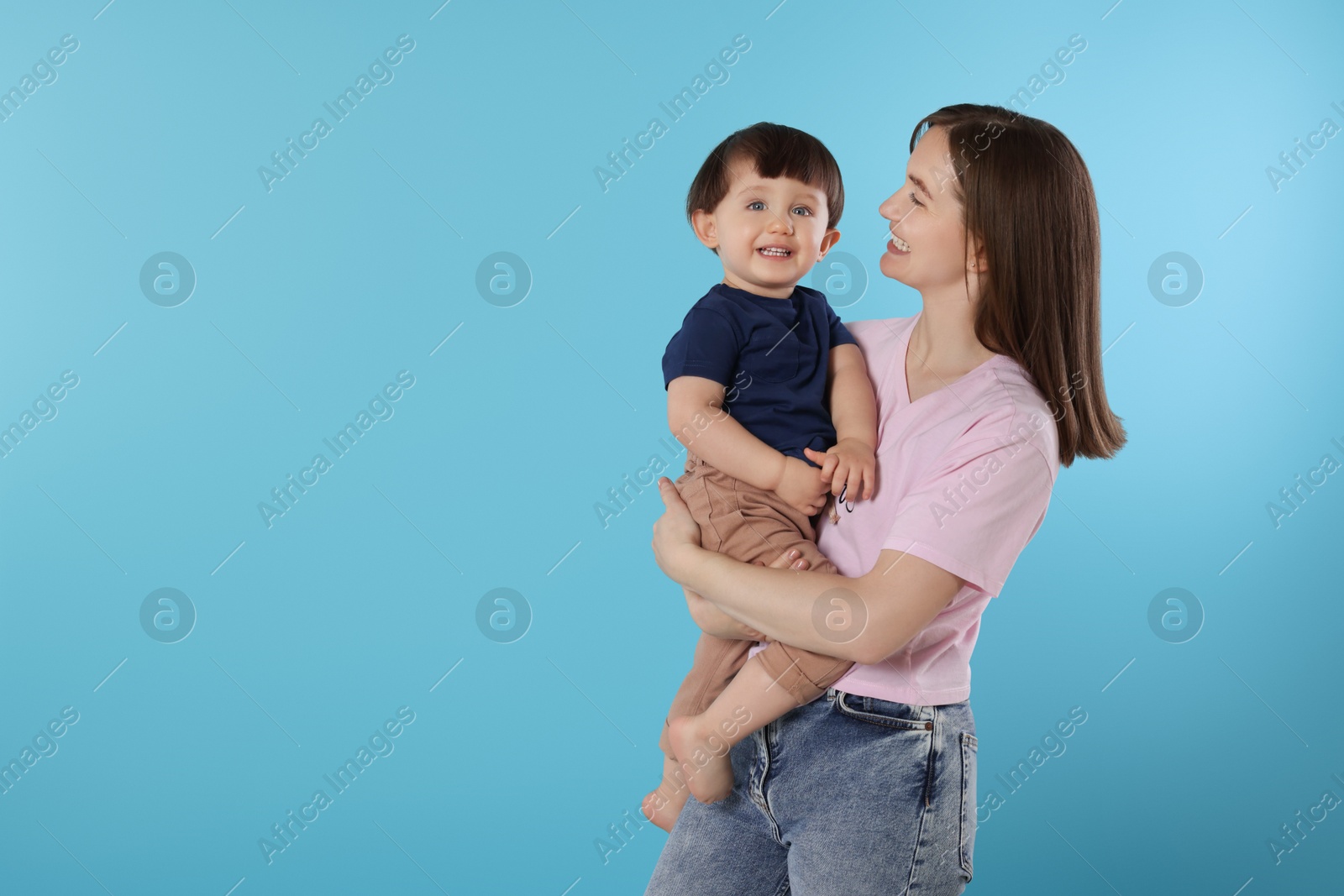 Photo of Happy mother with her cute little son on light blue background, space for text