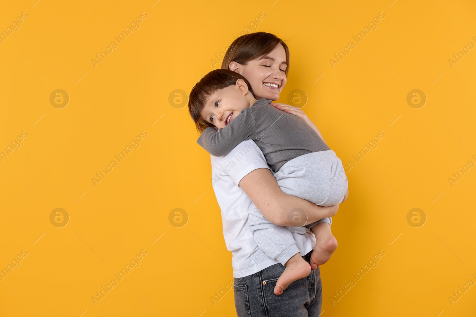 Photo of Happy mother with her cute little son on yellow background, space for text