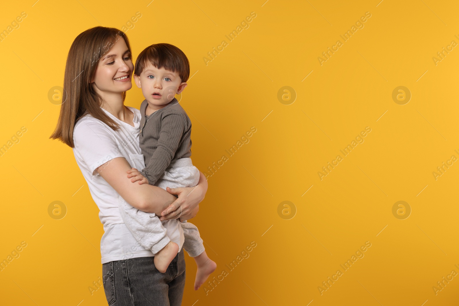 Photo of Happy mother with her cute little son on yellow background, space for text