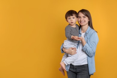 Happy mother with her cute little son on yellow background, space for text