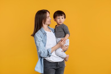 Photo of Happy mother with her cute little son on yellow background, space for text