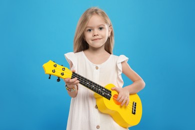 Photo of Little girl playing ukulele on light blue background