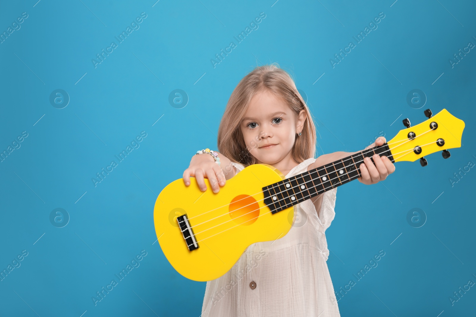 Photo of Little girl with ukulele on light blue background, space for text