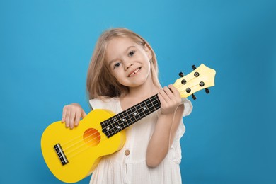 Photo of Little girl with ukulele on light blue background