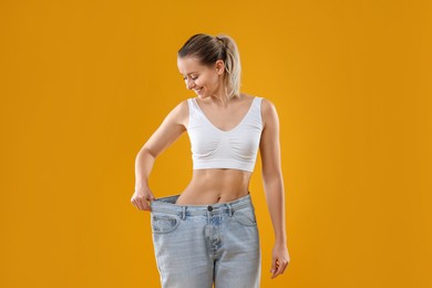 Photo of Weight loss. Happy woman wearing big jeans on yellow background