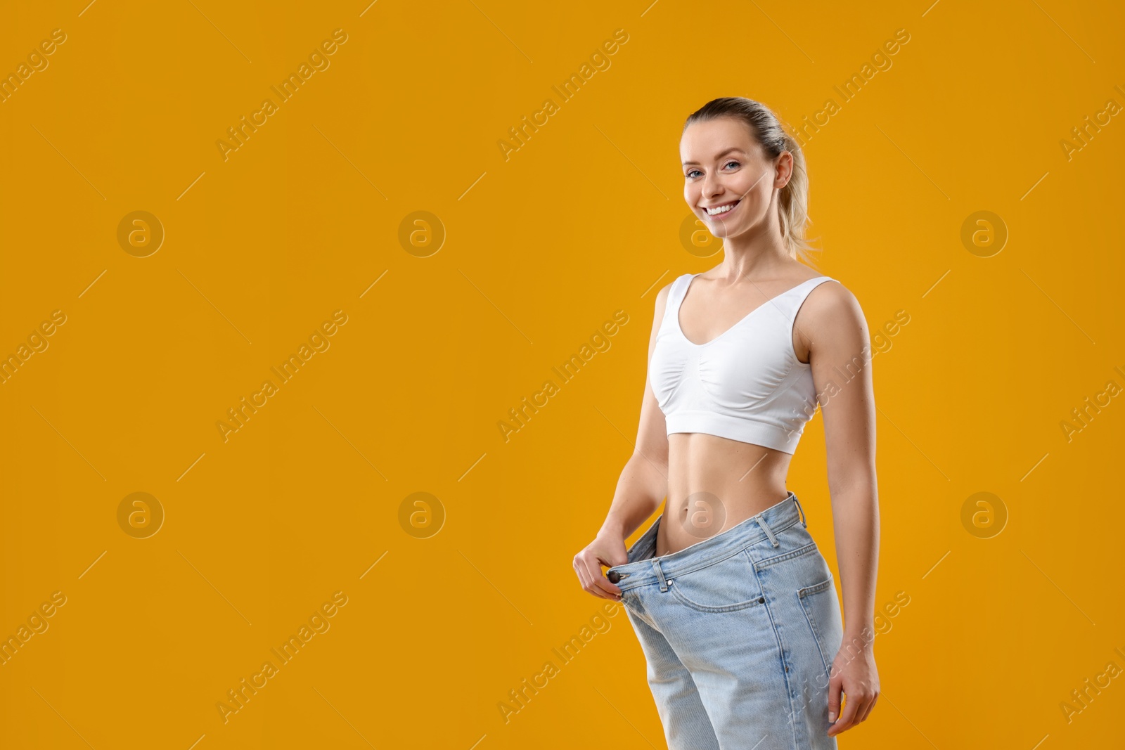 Photo of Weight loss. Happy woman wearing big jeans on yellow background, space for text