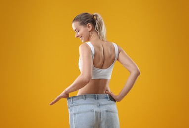 Photo of Weight loss. Happy woman wearing big jeans on yellow background