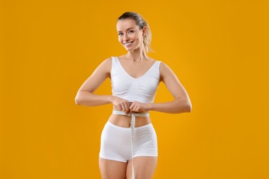 Weight loss. Happy woman measuring her slim waist with tape on yellow background