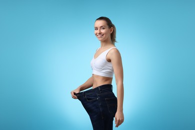 Photo of Weight loss. Happy woman wearing big jeans on light blue background