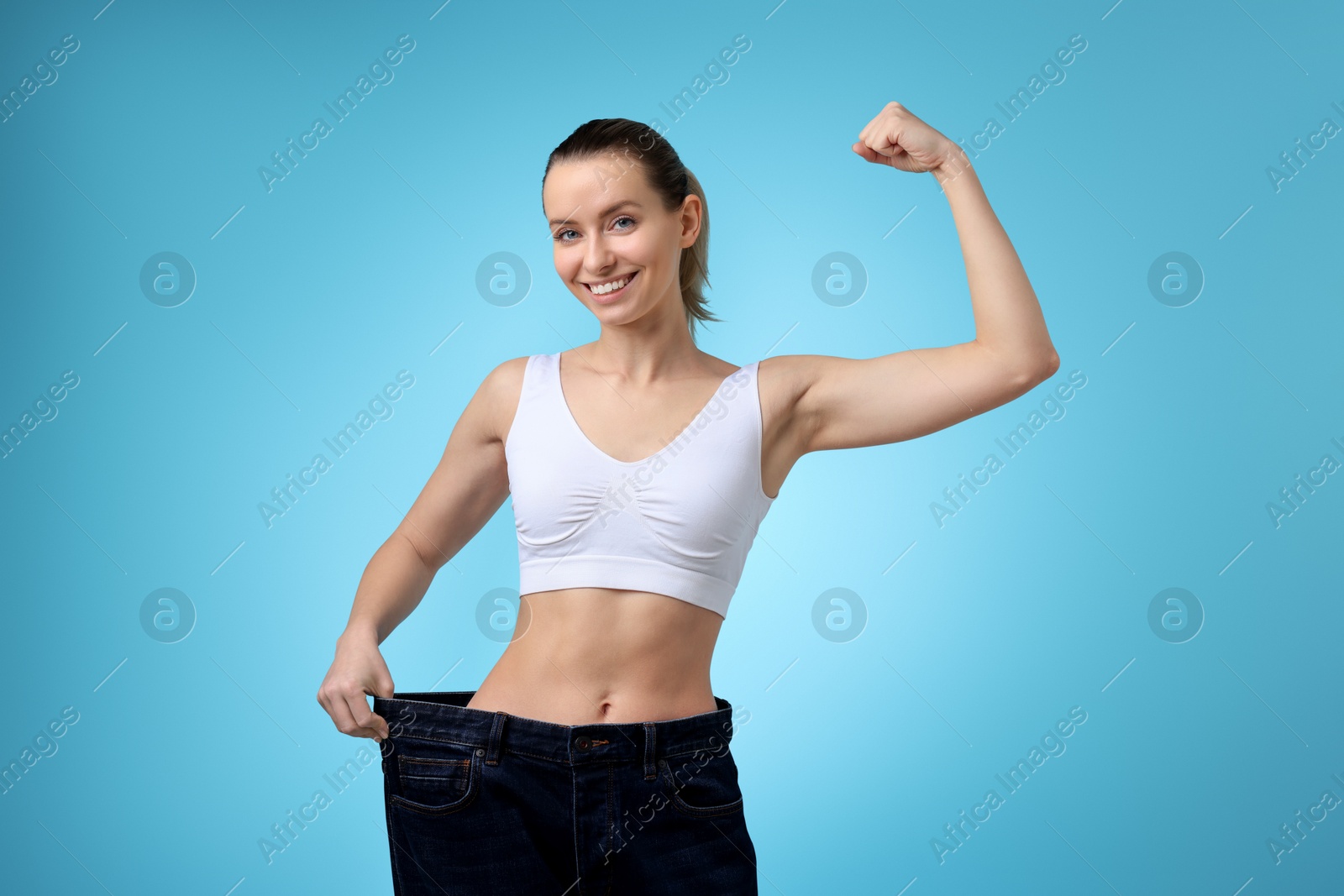 Photo of Weight loss. Happy woman wearing big jeans on light blue background