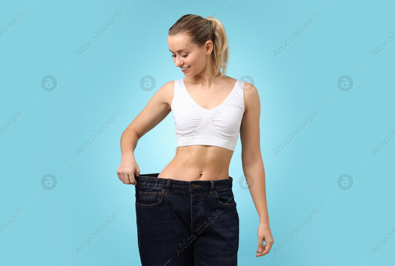 Photo of Weight loss. Happy woman wearing big jeans on light blue background