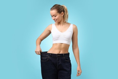 Photo of Weight loss. Happy woman wearing big jeans on light blue background