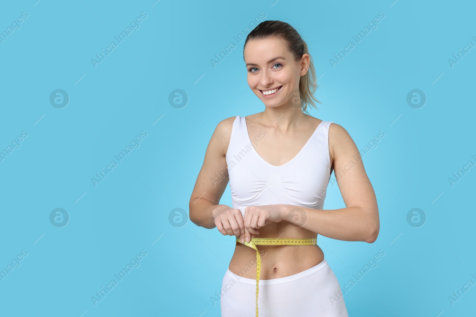 Photo of Weight loss. Happy woman measuring her slim waist with tape on light blue background, space for text