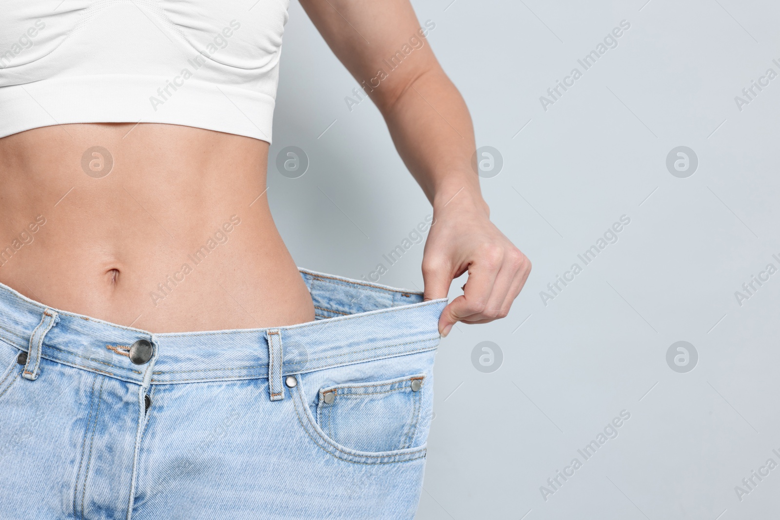 Photo of Weight loss. Woman wearing big jeans on light grey background, closeup. Space for text