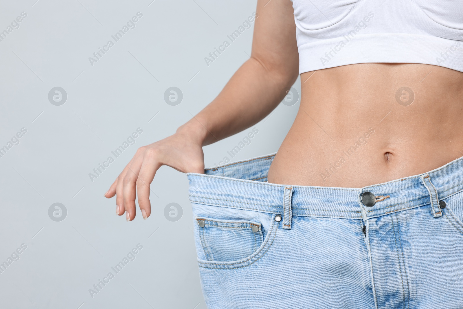 Photo of Weight loss. Woman wearing big jeans on light grey background, closeup. Space for text