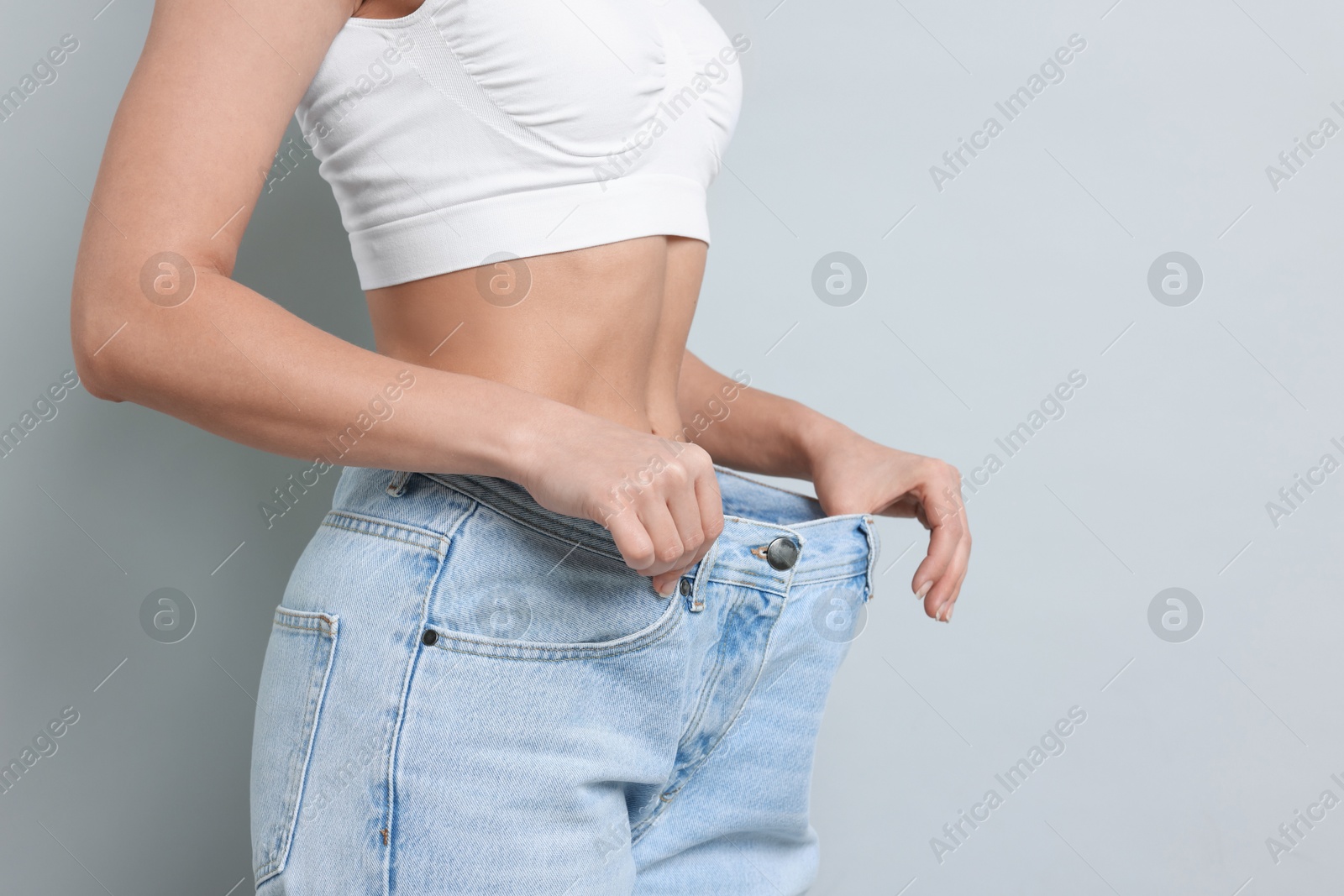 Photo of Weight loss. Woman wearing big jeans on light grey background, closeup. Space for text