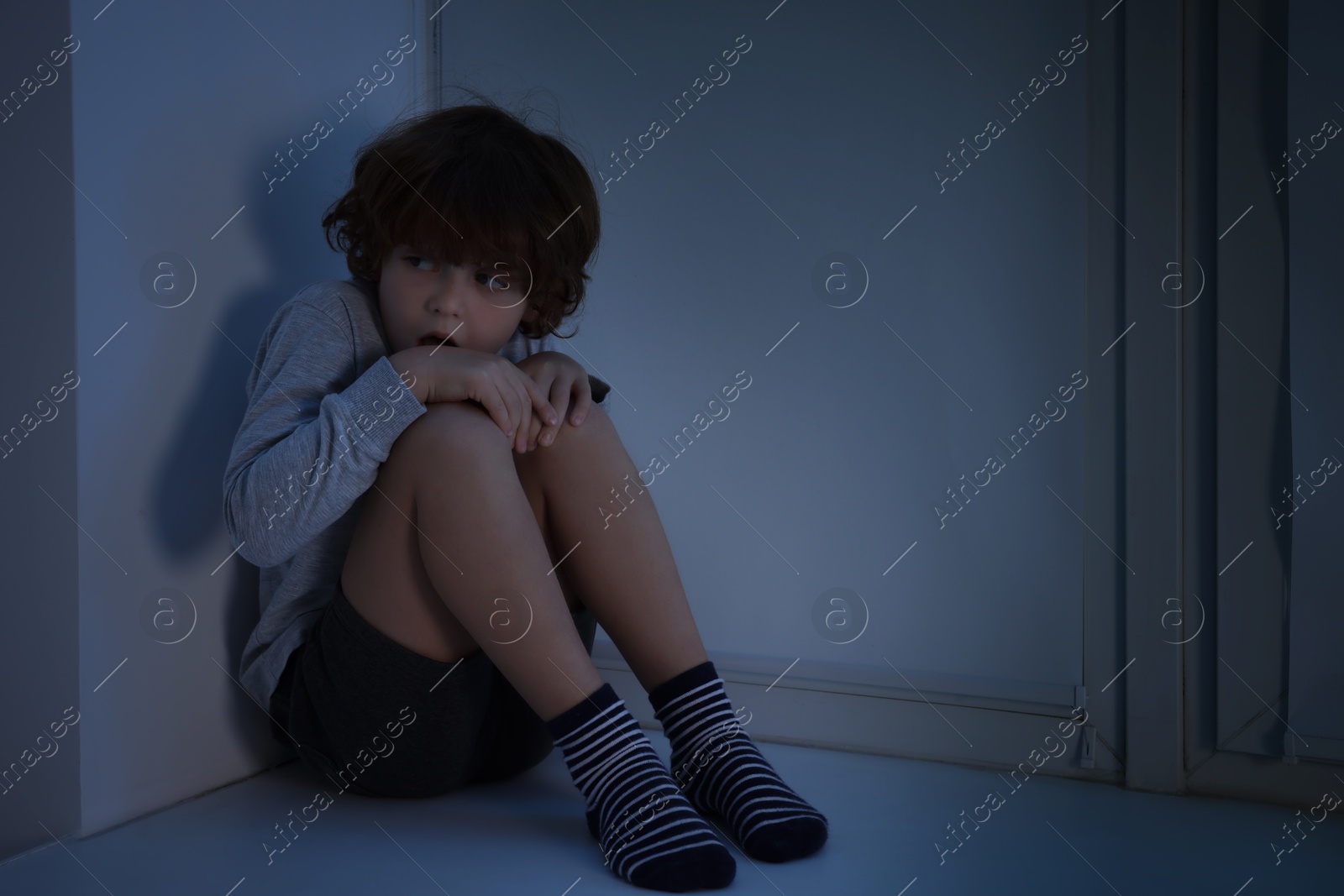 Photo of Fearful boy hiding on windowsill at night. Space for text