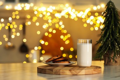 Photo of Glass of milk and tasty chocolate chip cookies on table against blurred Christmas lights. Bokeh effect