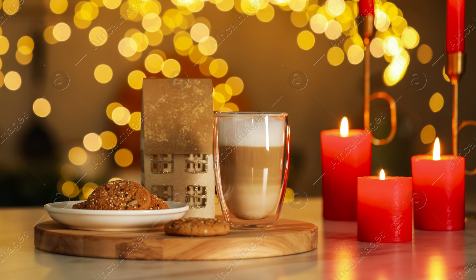 Photo of Aromatic coffee in glass, tasty cookies and burning candles on table against blurred Christmas lights. Bokeh effect