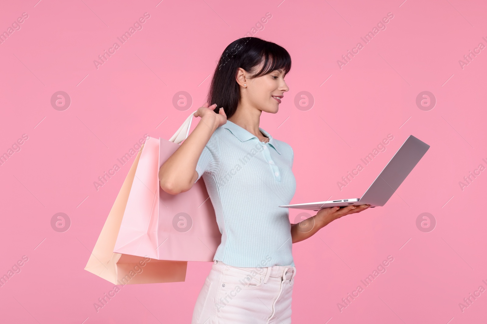 Photo of Internet shopping. Happy woman with laptop and colorful bags on pink background