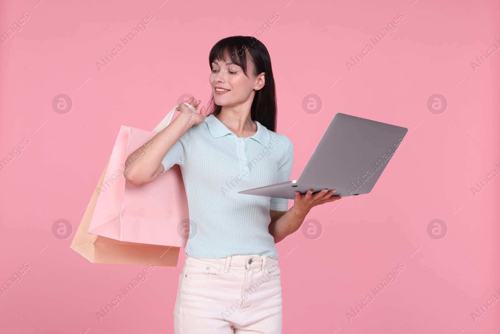 Photo of Internet shopping. Happy woman with laptop and colorful bags on pink background