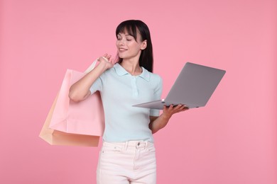 Photo of Internet shopping. Happy woman with laptop and colorful bags on pink background