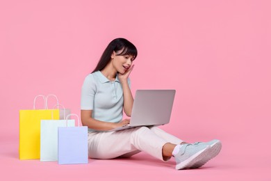 Photo of Internet shopping. Happy woman with laptop and colorful bags on pink background