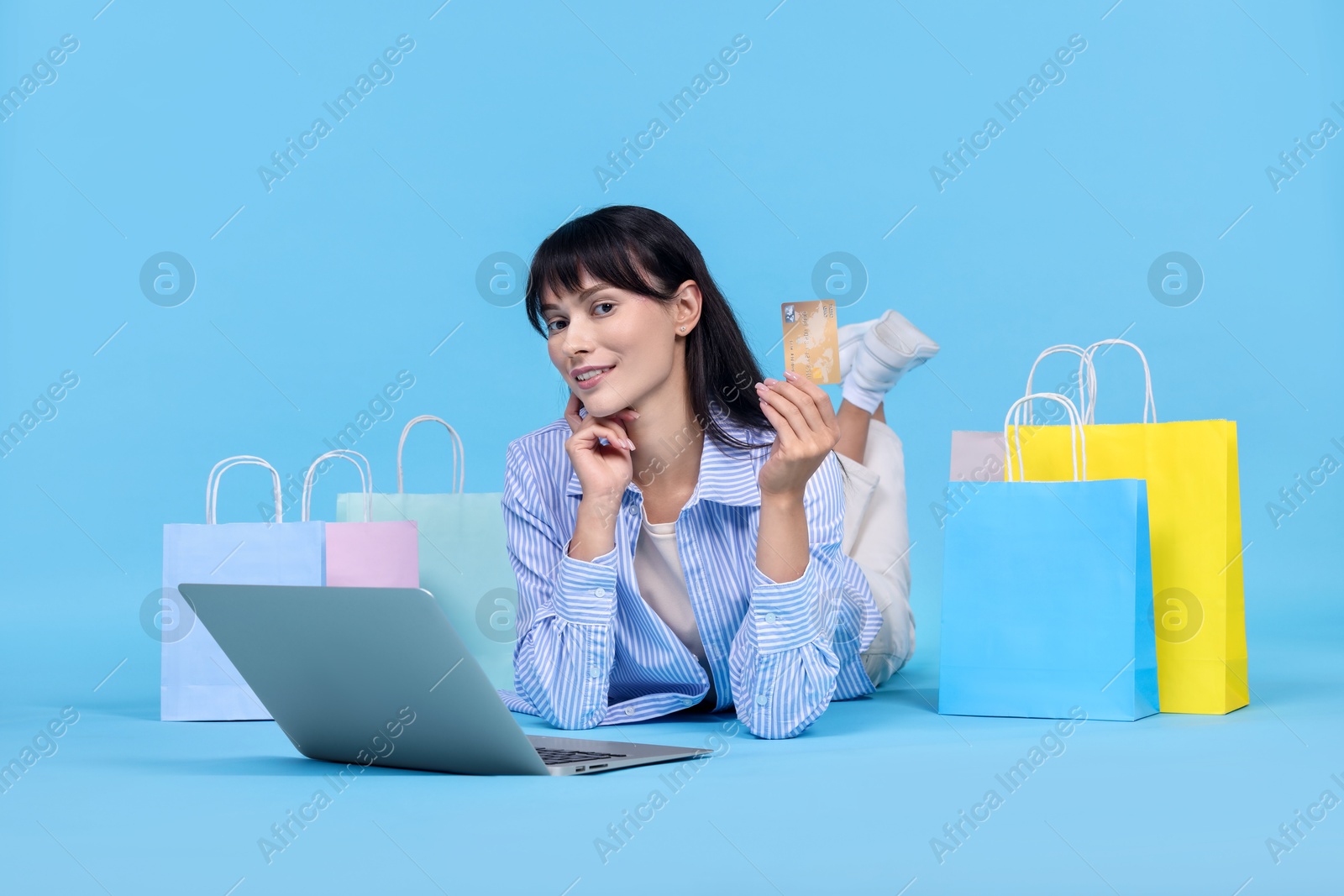 Photo of Internet shopping. Happy woman with credit card, laptop and colorful bags on light blue background