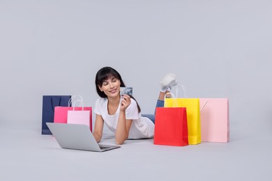 Photo of Internet shopping. Happy woman with credit card, laptop and colorful bags on grey background