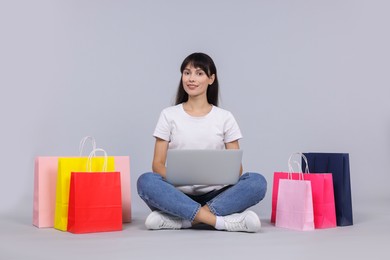 Photo of Internet shopping. Happy woman with laptop and colorful bags on grey background