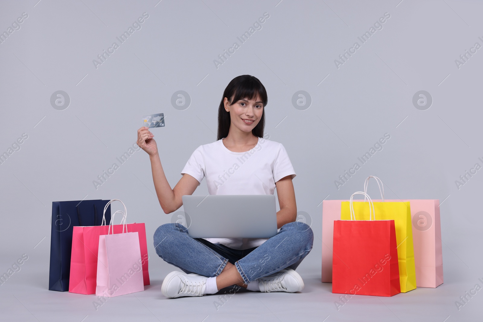 Photo of Internet shopping. Happy woman with credit card, laptop and colorful bags on grey background