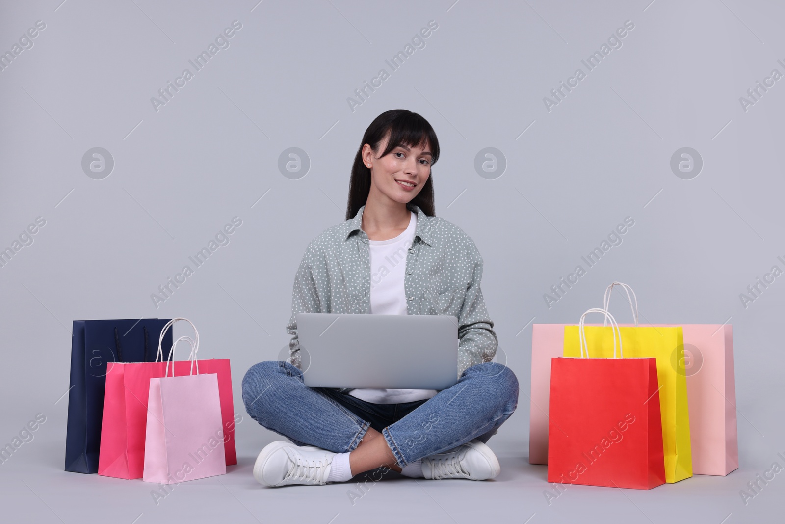 Photo of Internet shopping. Happy woman with laptop and colorful bags on grey background