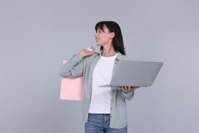 Photo of Internet shopping. Happy woman with laptop and colorful bags on grey background